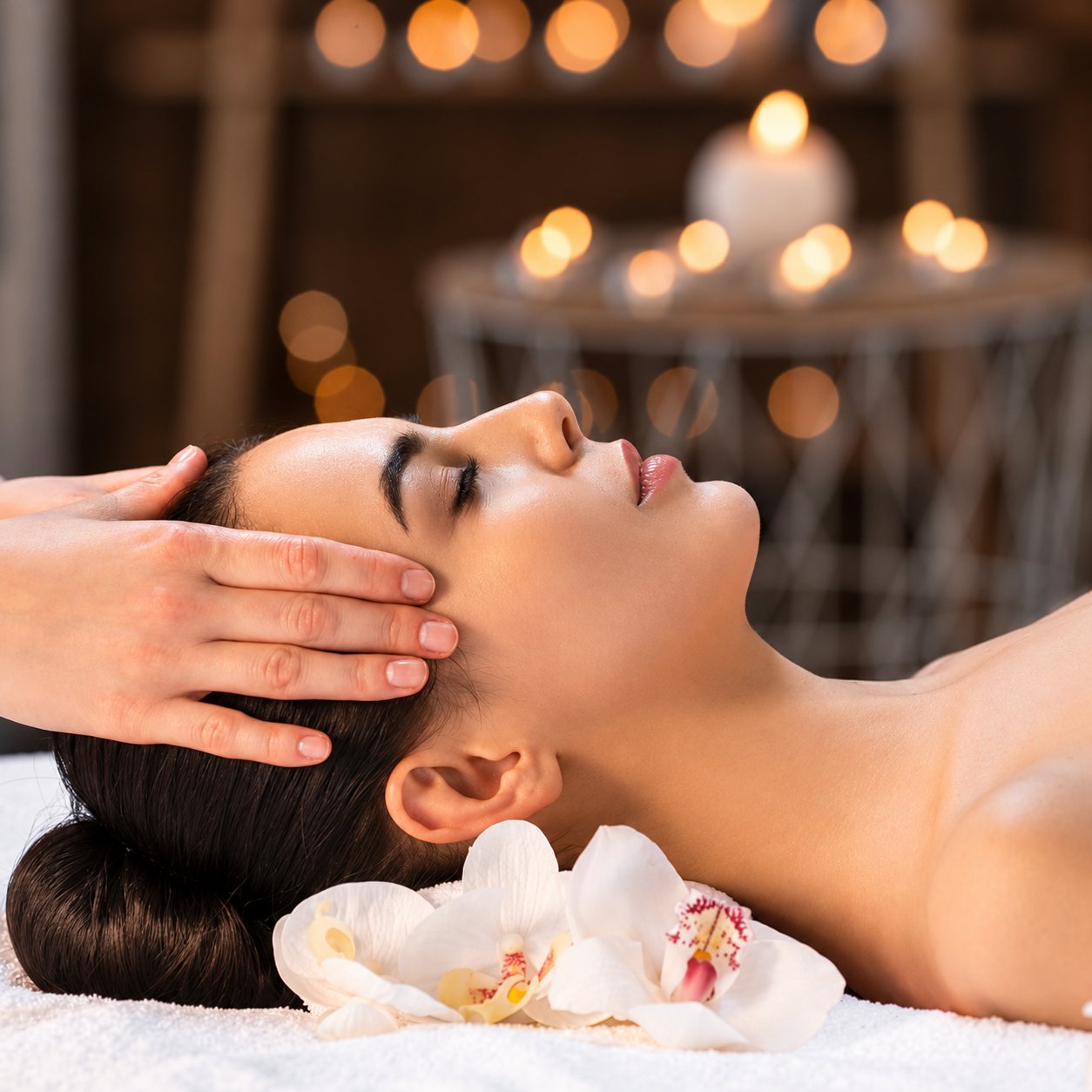 Femme recevant un massage du visage dans un spa, orchidées blanches.