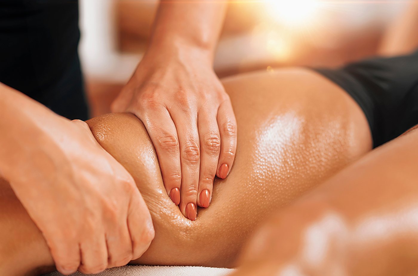 Gros plan sur des mains qui massent une cuisse à l’huile.