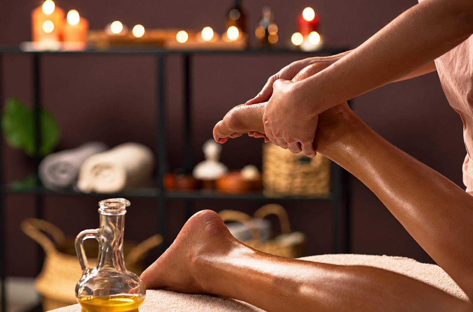 Massage des pieds à l’huile dans une ambiance de spa éclairée aux bougies.