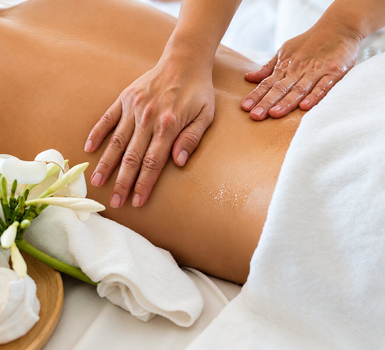 Massage du dos à l’huile, fleurs blanches et serviettes.