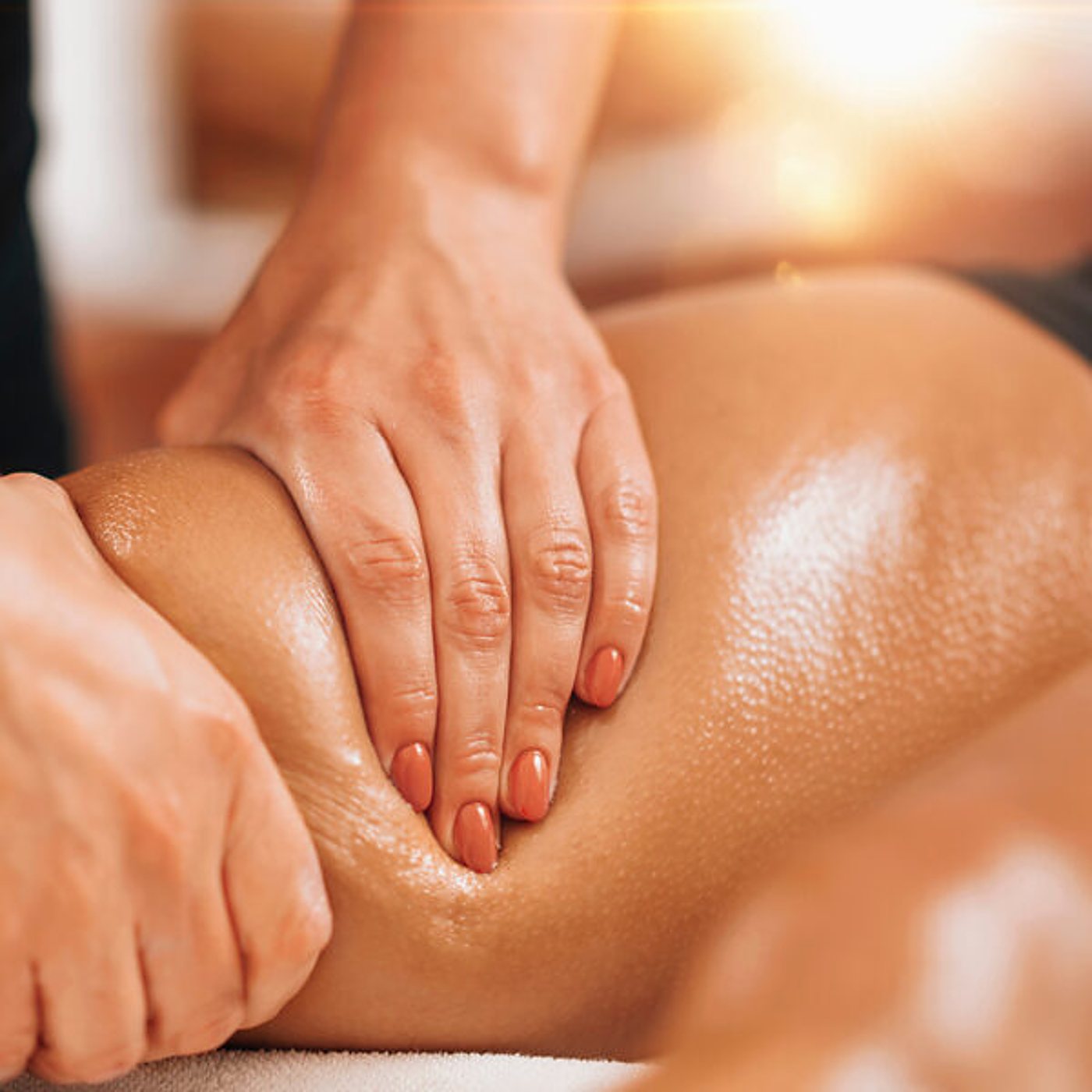 Mains d’une praticienne massant une jambe à l’huile.