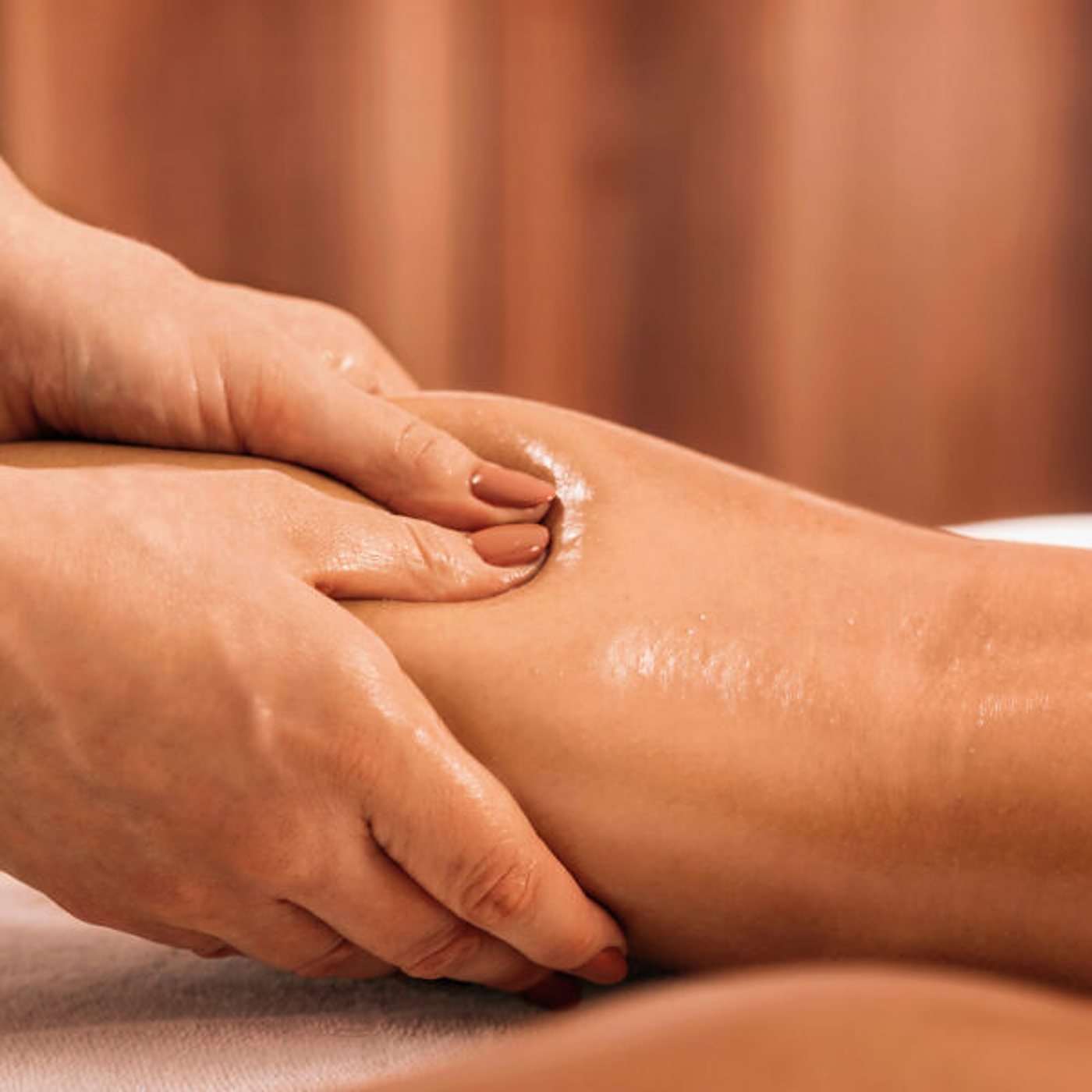 Mains d’une praticienne sur une jambe huilée.